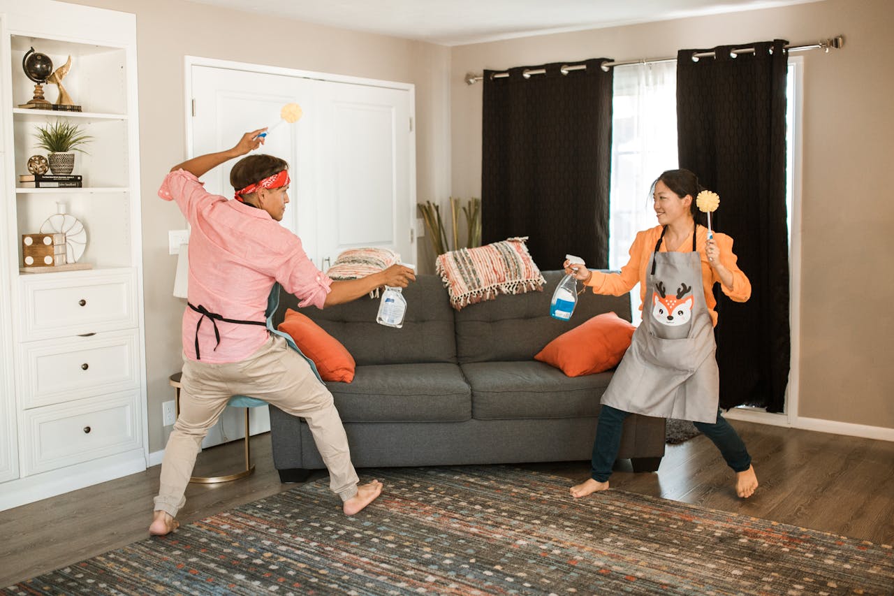 about-02 A joyful couple engages in a playful cleaning fight in their living room, showcasing light-hearted domestic life.