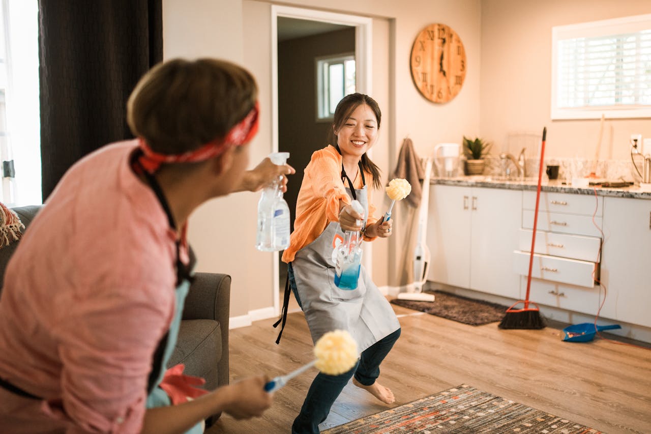 hero-img-01 Asian couple having fun while cleaning their home, enhancing a cheerful atmosphere.